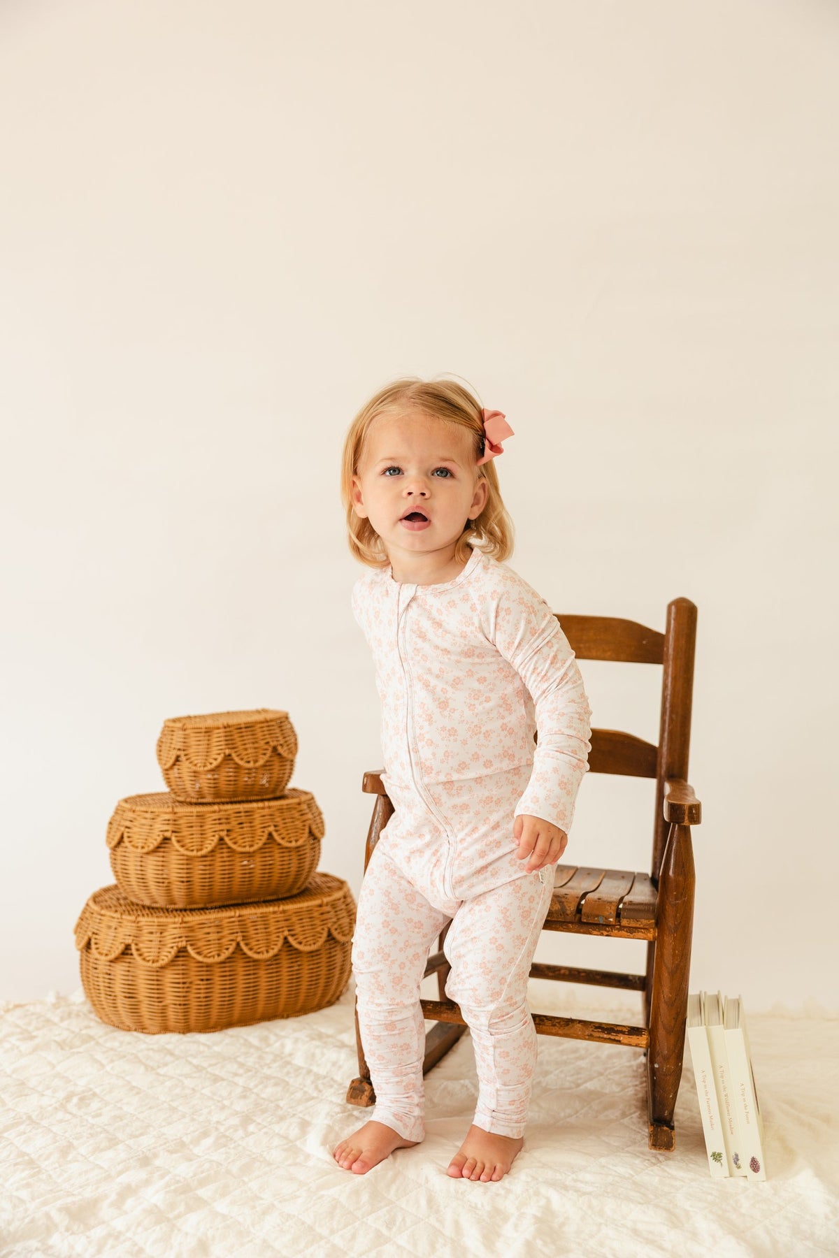 Toddler standing by a wooden chair in the Blush Blossoms sleeper