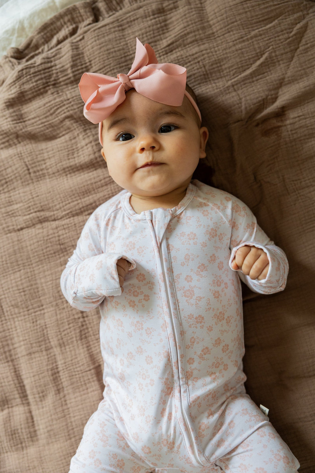 Baby with a pink bow lying down in the Blush Blossoms sleeper