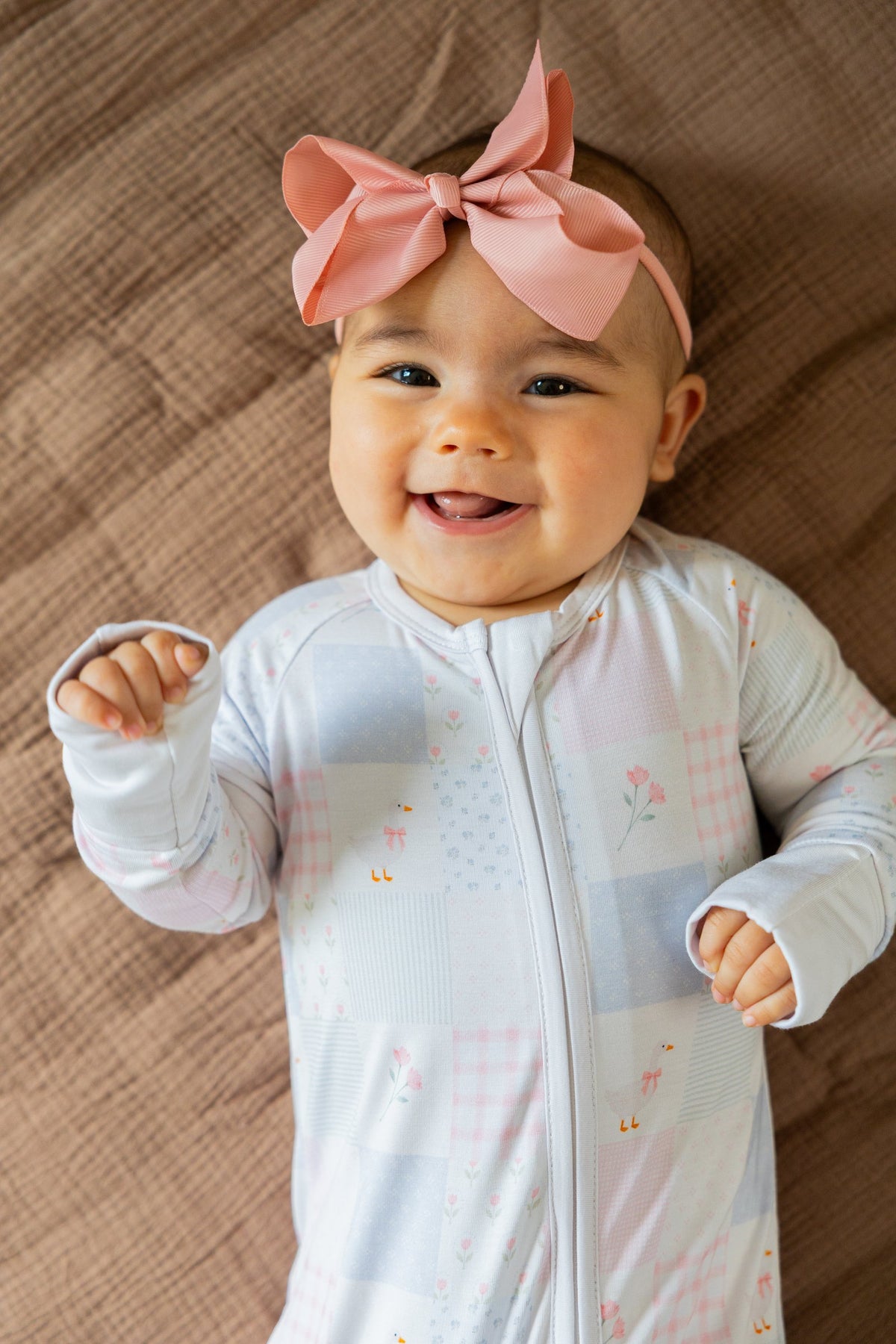 Smiling baby lying on a blanket in the Heirloom Quilt sleeper