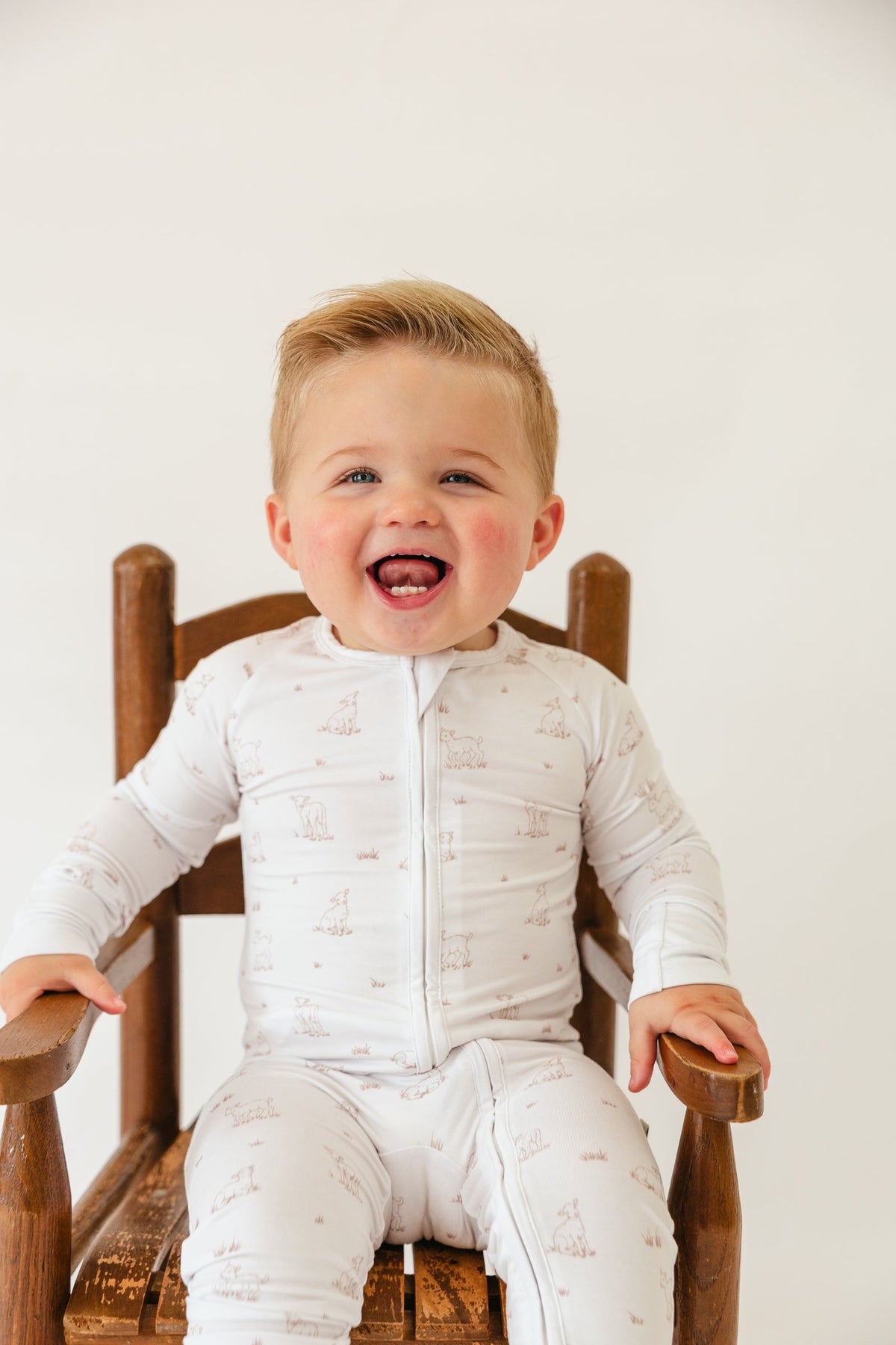 Toddler sitting in a wooden chair wearing the Little Lamb sleeper