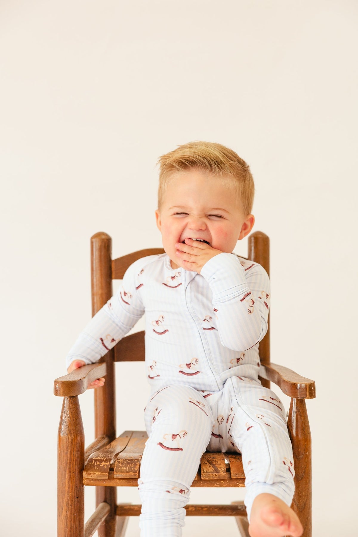 Laughing toddler in a wooden chair wearing the Rocking Horse sleeper