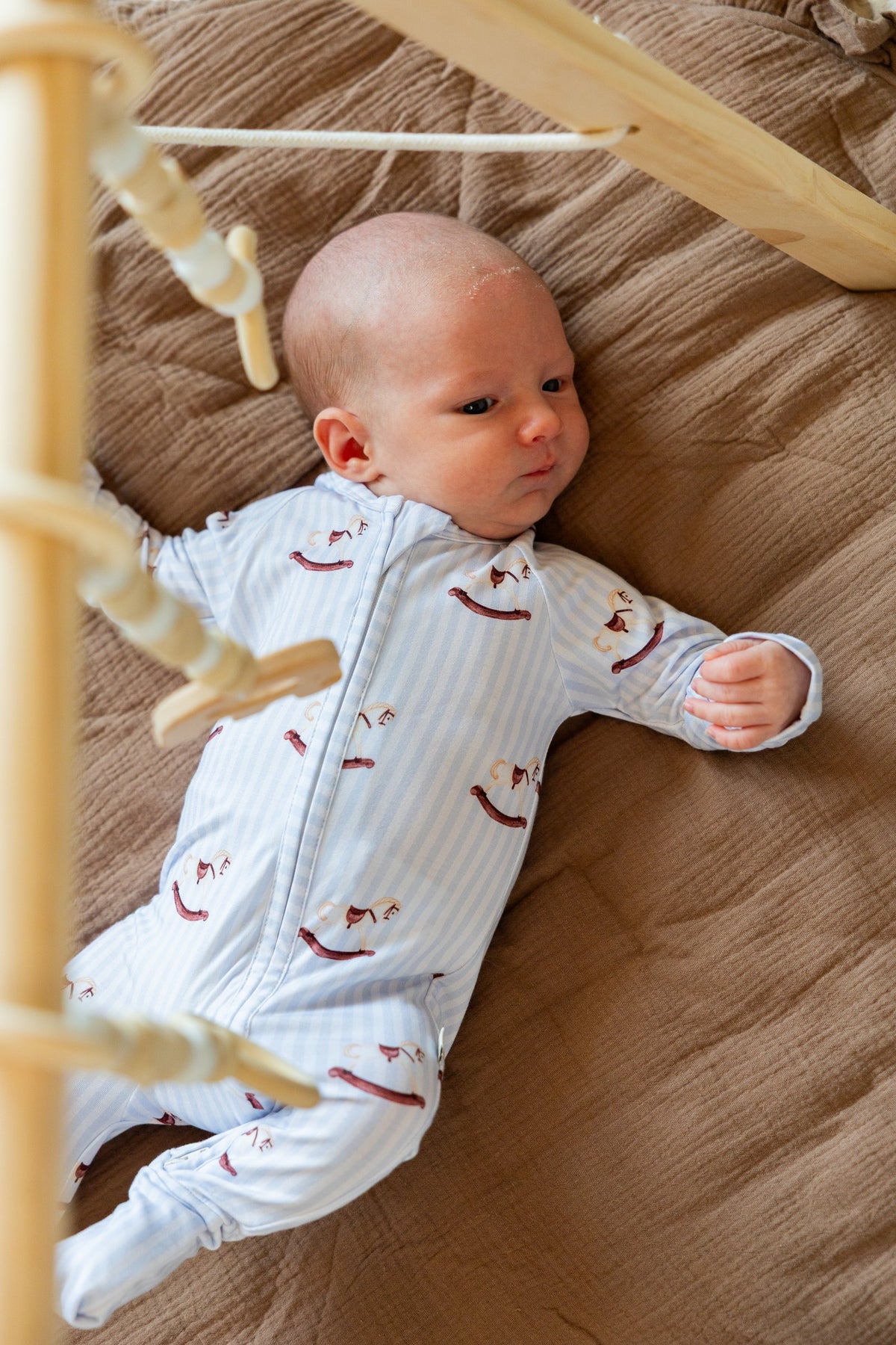 Newborn lying under a play gym in the footed Rocking Horse sleeper