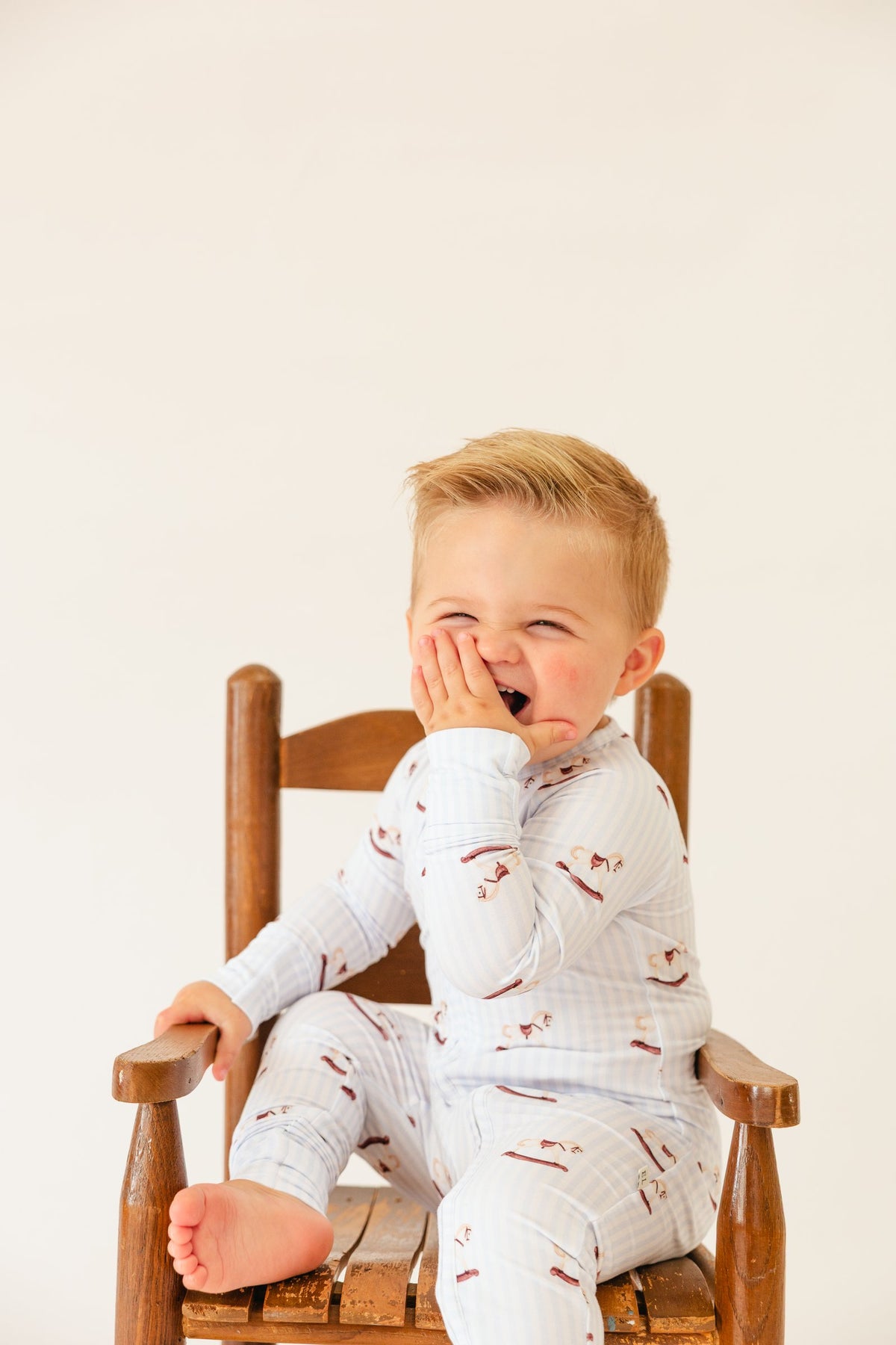 Laughing toddler in a wooden chair wearing the Rocking Horse sleeper